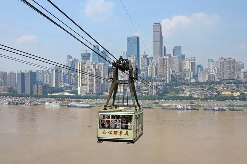 A cable car moving over a river with a city skyline in the background. 2