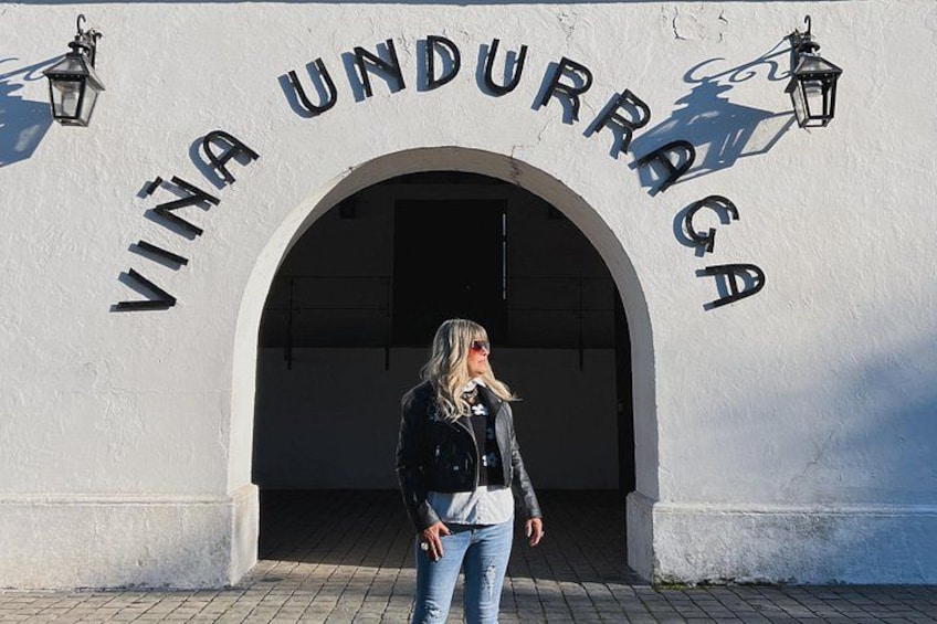 A person standing in front of a building with an arched entrance and the words 'VINA UNDURRAGA' on the wall. 1