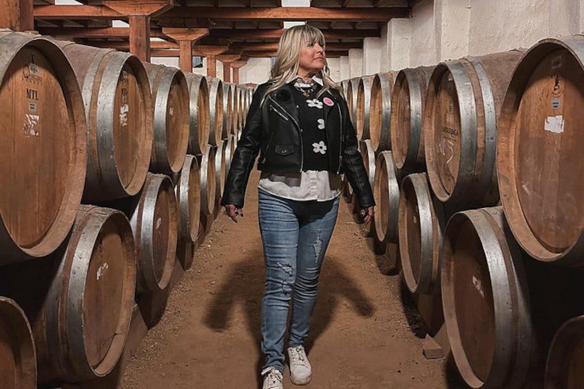 A person walking between rows of wooden wine barrels in a cellar. 3