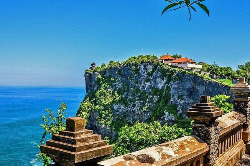 A coastal cliff with a traditional building on top, a stone balustrade, and a clear blue sea. 4