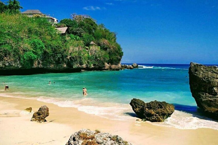 A beach with clear turquoise water, rocky outcrops, and lush greenery. 1