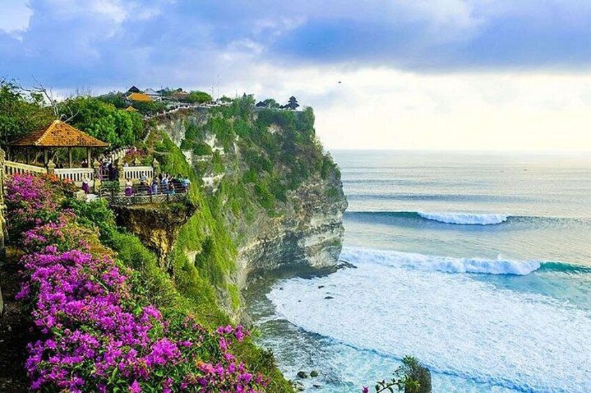 A coastal cliff with a building and purple flowers. 3