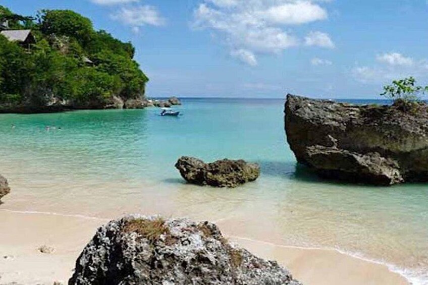 A beach with clear turquoise water, large rocks, and a small boat in the distance. 2