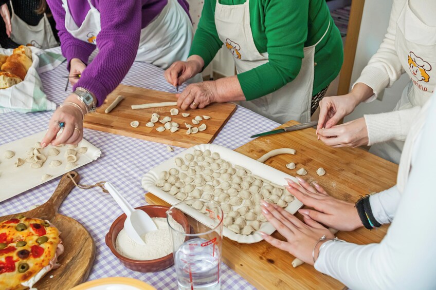 People preparing food, specifically dough, on a checkered tablecloth. 3