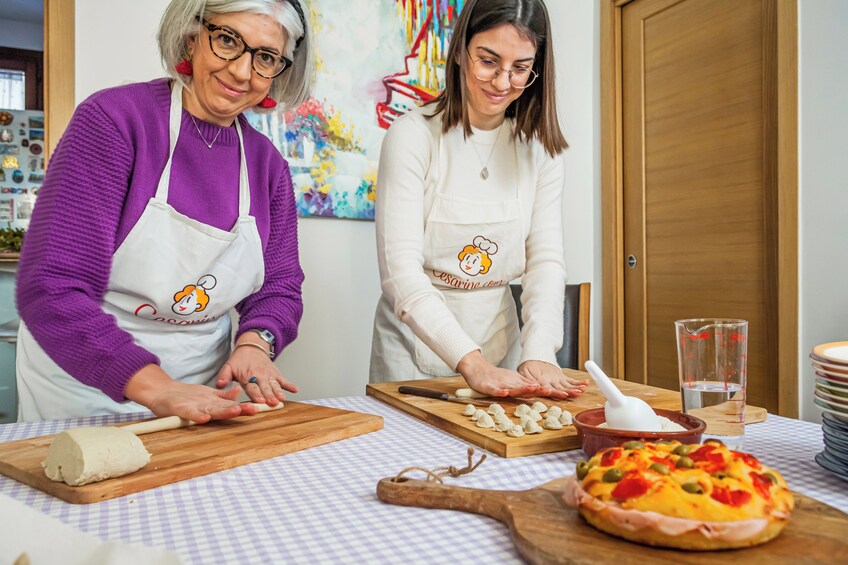 Two people preparing food, one rolling dough and the other cutting vegetables, with a pizza on the table. 5