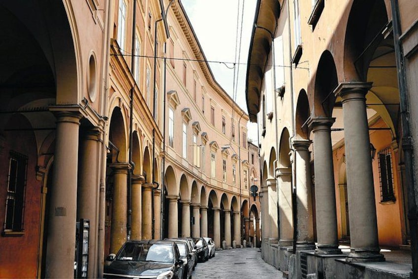 A street with parked cars, arches, and buildings. 3
