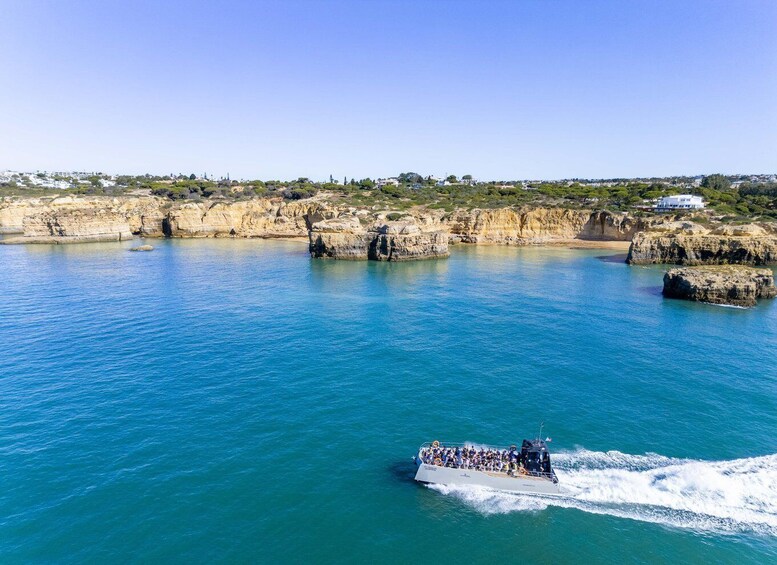 A boat with passengers on a clear day near rocky cliffs and a coastal town. 5