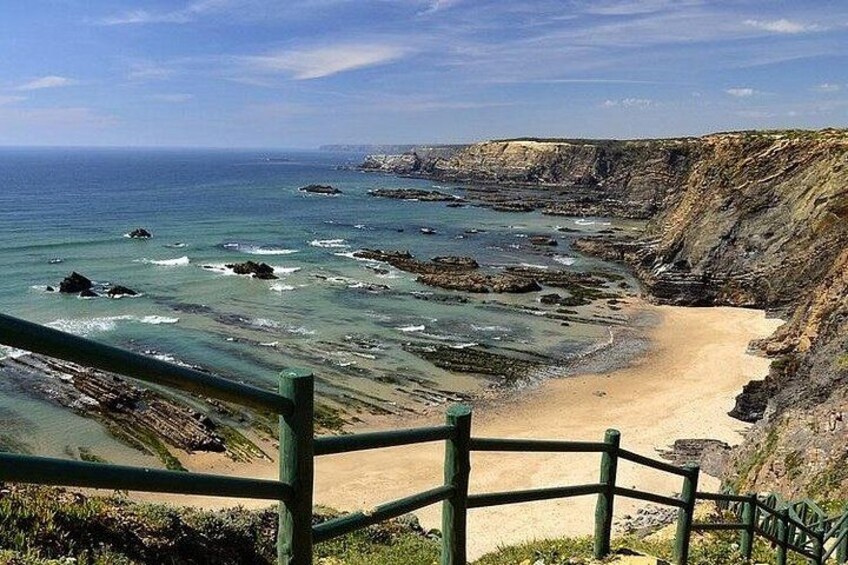 A coastal landscape with a sandy beach, rocky cliffs, and a wooden fence. 5