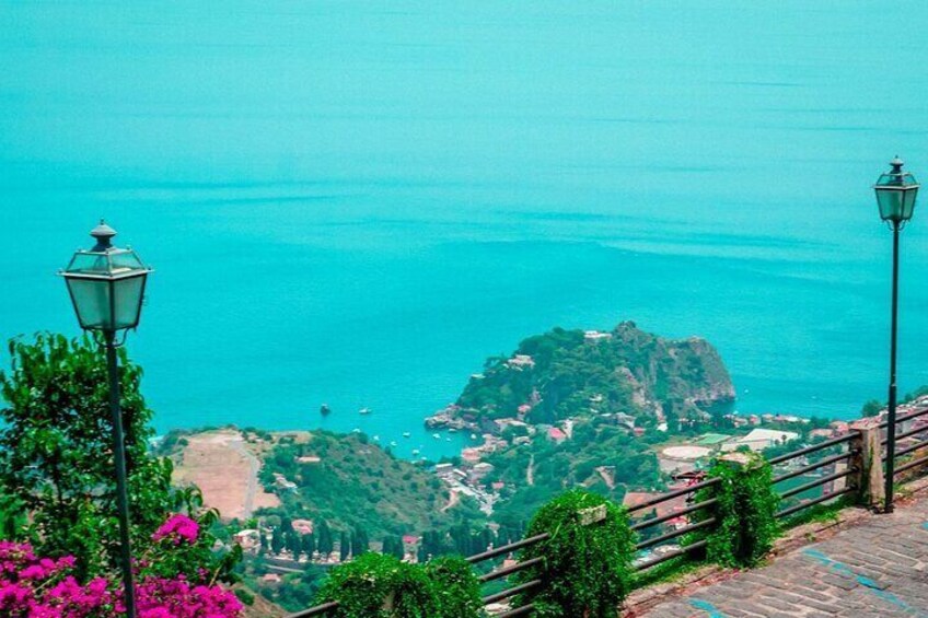 A coastal landscape with a prominent rocky island, a paved pathway, and a street lamp. 2
