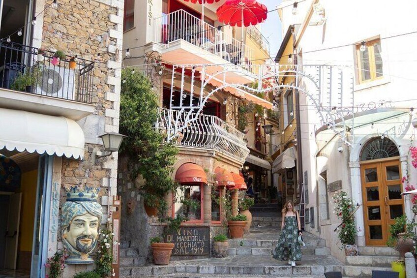 A narrow street with a staircase leading to a building with balconies adorned with red umbrellas. 5