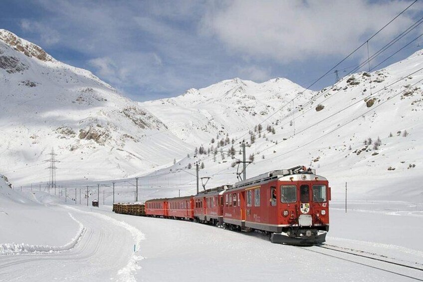 Un train rouge circule sur des voies ferrées dans une région montagneuse enneigée. 2