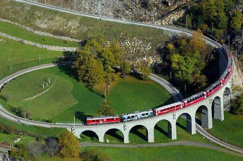 Un train sur un pont blanc à arcades, entouré de champs verdoyants et d’arbres. 4