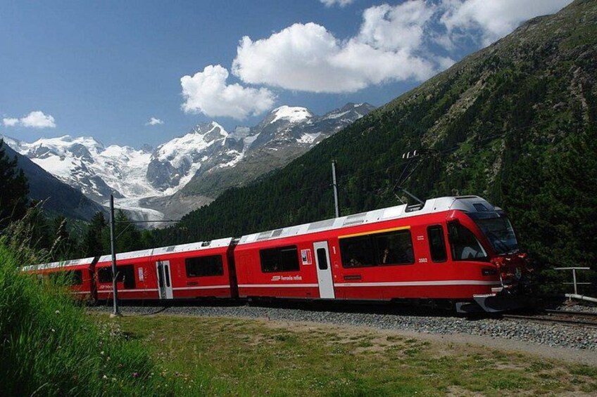 Un train rouge circule sur des voies ferrées, avec des montagnes enneigées en arrière-plan. 3