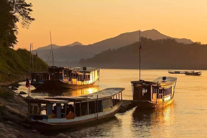 Un río con barcos amarrados a la orilla, una montaña al fondo y un atardecer. 3