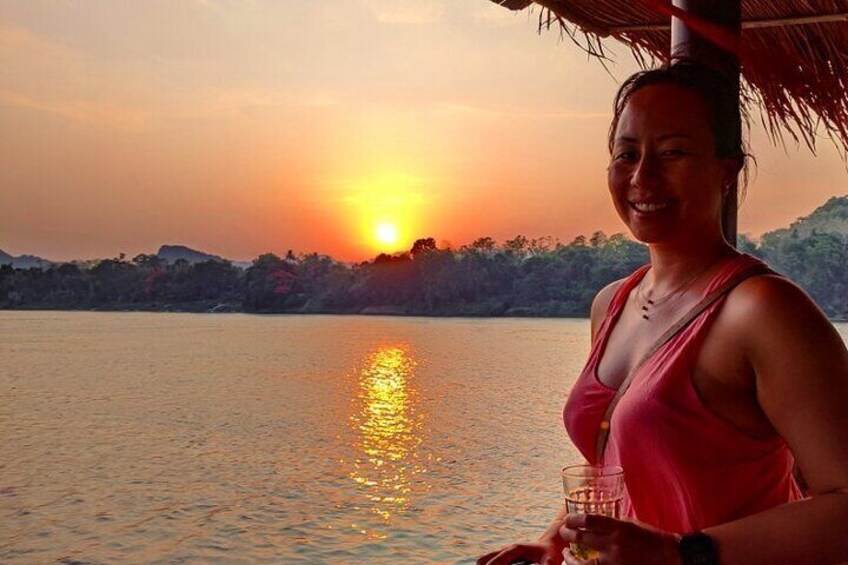 Una puesta de sol sobre un cuerpo de agua con una persona sosteniendo un vaso. 5