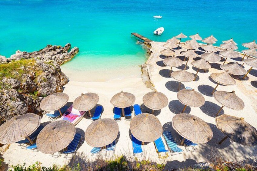 Una spiaggia con numerosi ombrelloni di paglia e poltrone blu. 5