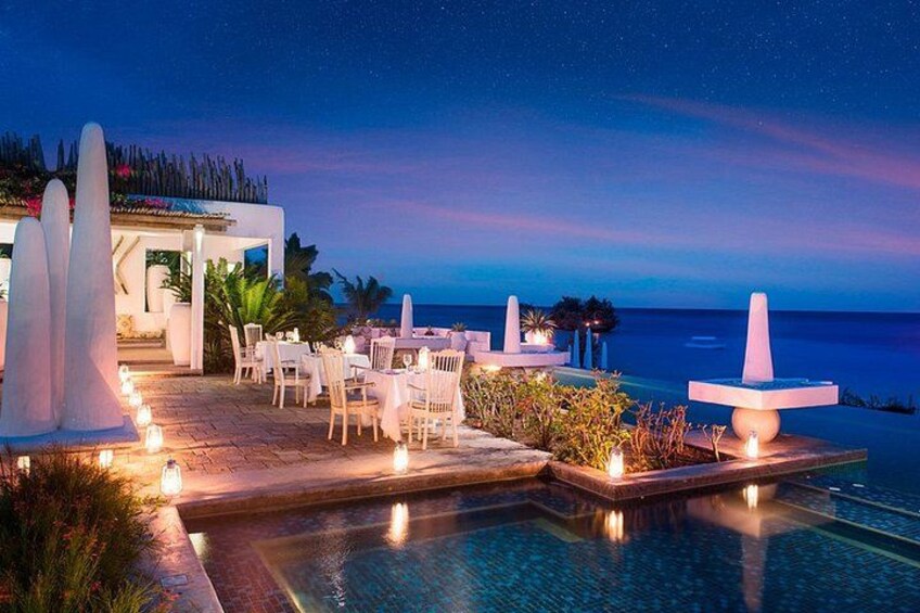 A poolside area with chairs and tables, a pool, and a view of the ocean at twilight. 3