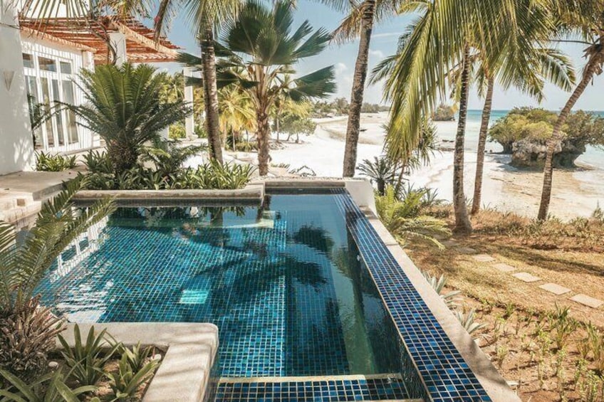 A swimming pool with blue tiles, surrounded by palm trees and a beach. 4