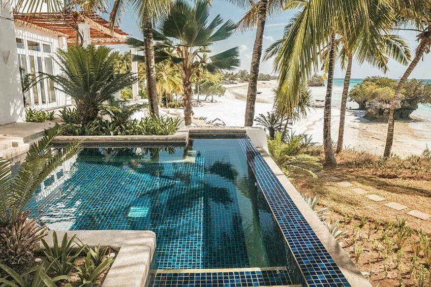 A swimming pool with blue tiles, surrounded by palm trees and a beach. 4