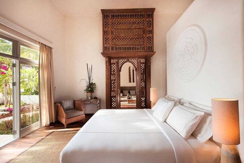 A hotel room with a large bed, a wooden partition, a chair, and a view of the outdoors. 5