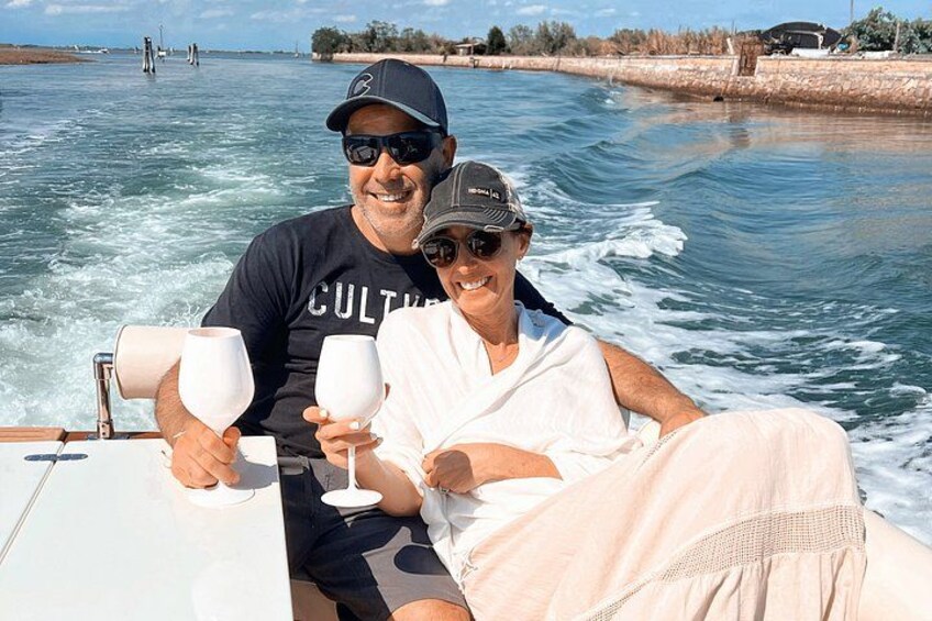 Two people on a boat, holding wine glasses, with water and a distant shoreline in the background. 4