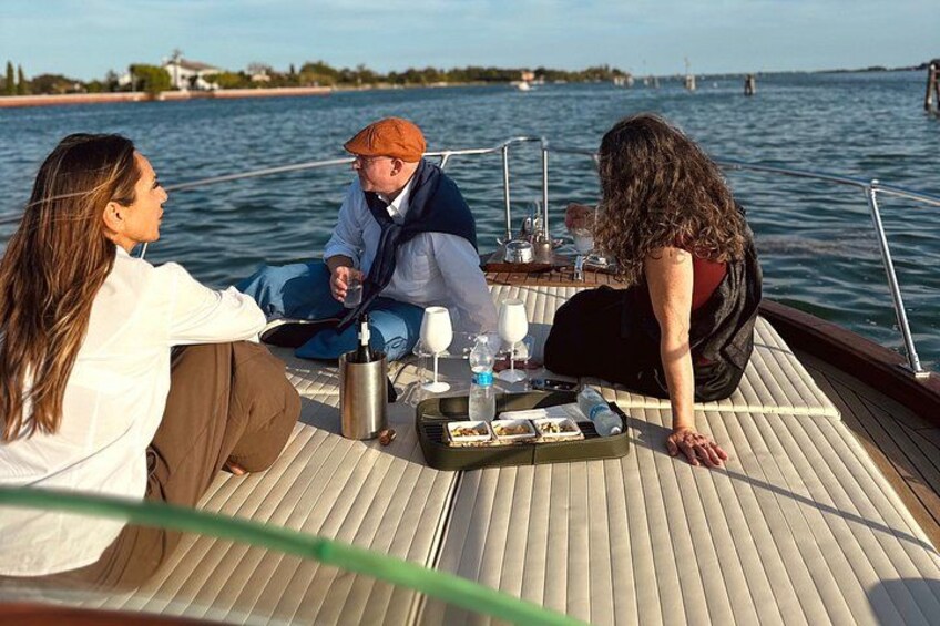 Three people on a boat with a table set for a meal, surrounded by water and a distant bridge. 3