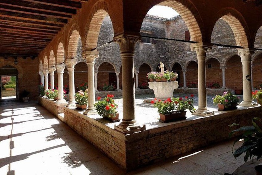 An arched courtyard with columns, potted plants, and a statue. 4