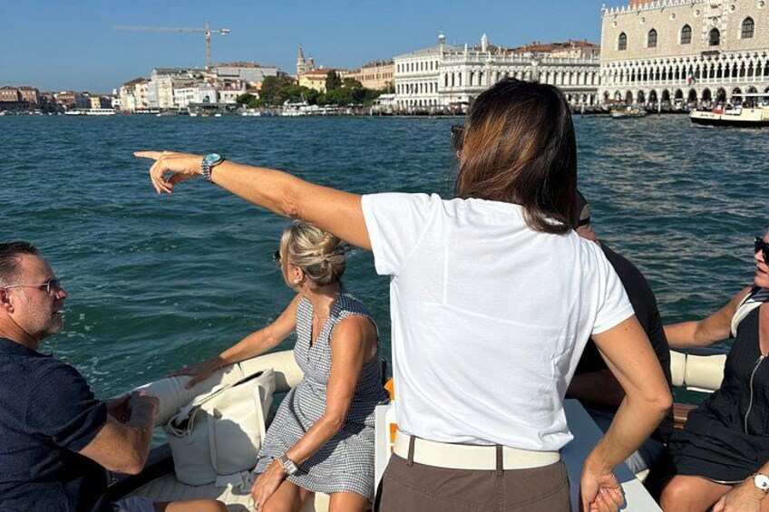 A group of people on a boat, pointing towards a historic building across the water. 2