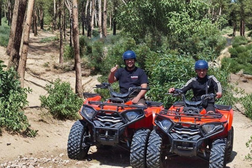 Two people on orange ATVs on a dirt path in a forested area. 2
