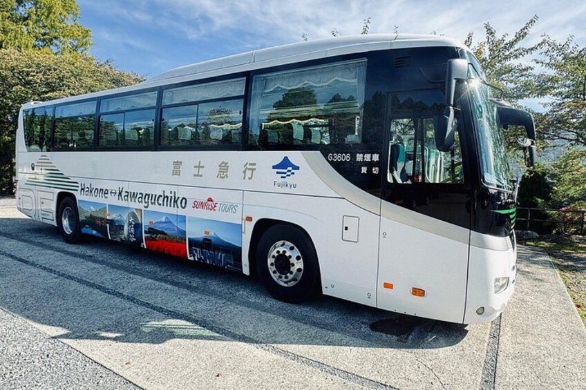 A white bus with 'Sunrise Tours' and 'Hakone & Kawaguchiko' branding, parked on a road with trees in the background. 1
