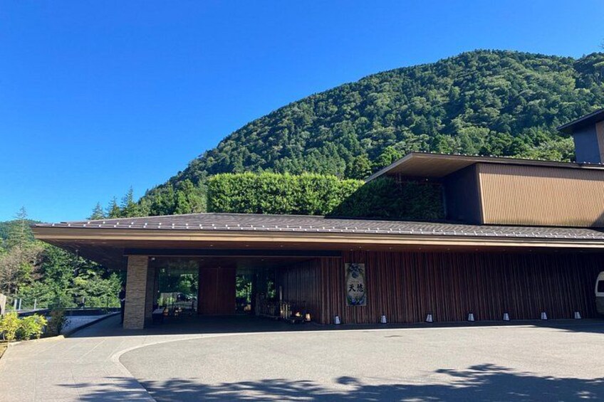 A modern building with a flat roof, surrounded by a paved area and a forested hill in the background. 4