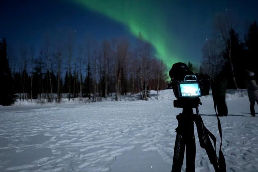 A camera on a tripod capturing the Northern Lights in a snowy landscape. 4