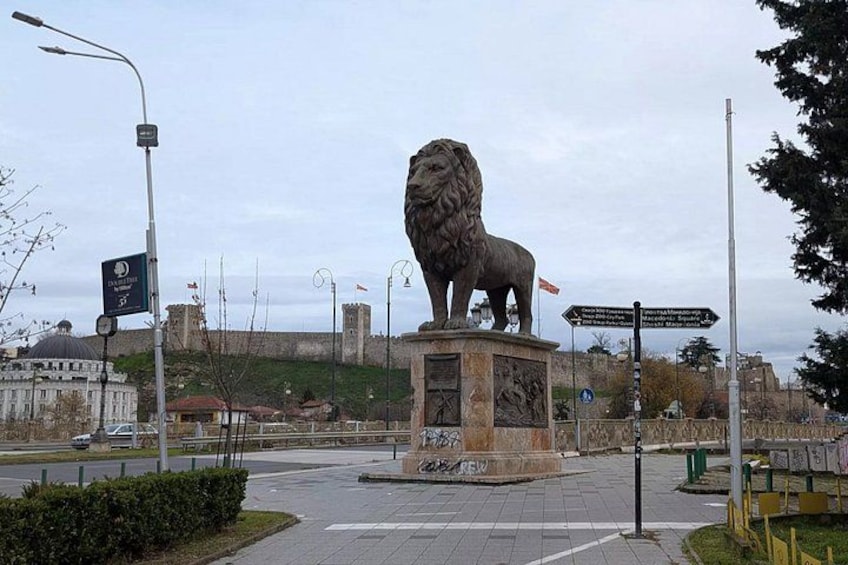 A lion statue on a pedestal in an urban setting with a castle in the background. 1