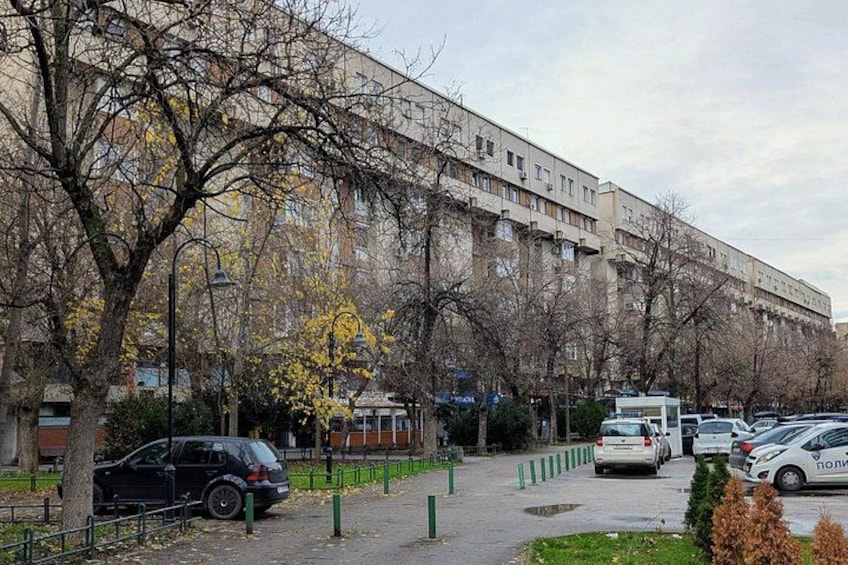 A parking lot with cars, a building with multiple windows, and leafless trees. 4