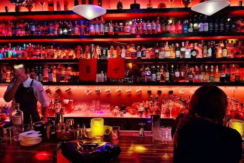 Eine Bar mit Regalen voller Flaschen und Gläsern, einem Barkeeper und einem Gast. 1
