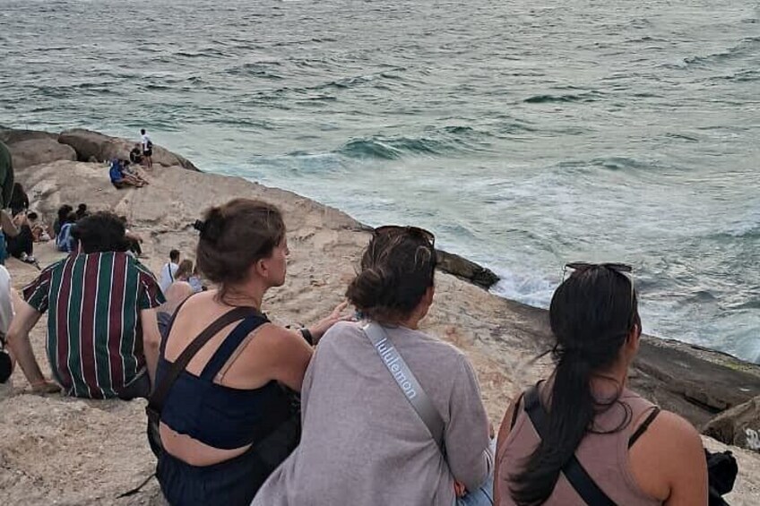 People sitting on a rocky beach, looking out at the ocean. 4