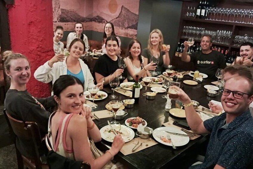 A group of people sitting around a table in a restaurant, with wine glasses and plates of food. 2
