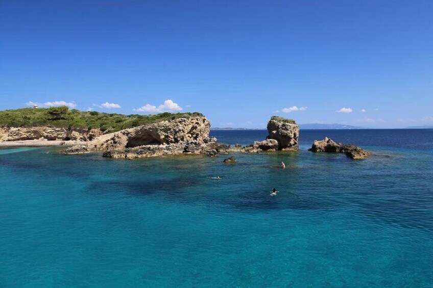 A coastal landscape with clear turquoise waters, rocky formations, and a distant shoreline. 3