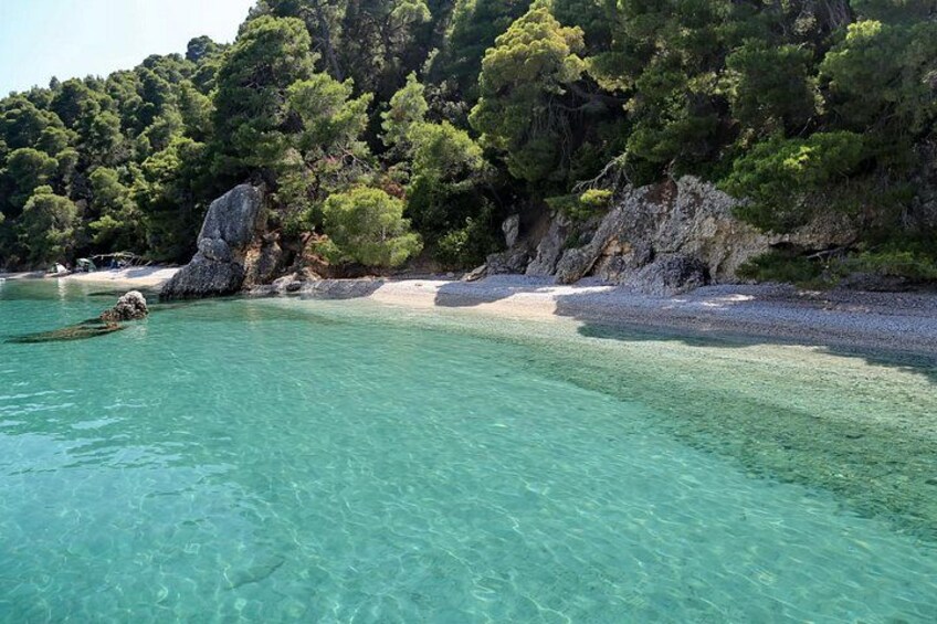 A clear turquoise sea, a sandy beach, and dense green trees on a rocky hillside. 5