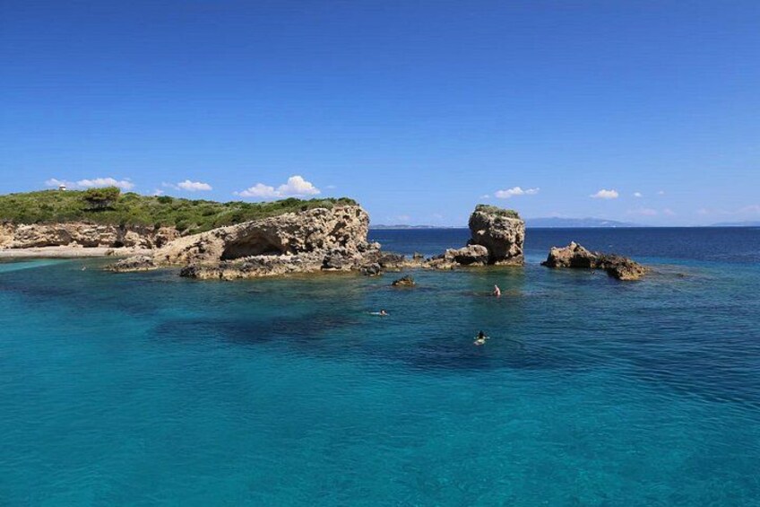 A coastal landscape with clear blue waters, rocky formations, and sparse vegetation. 3