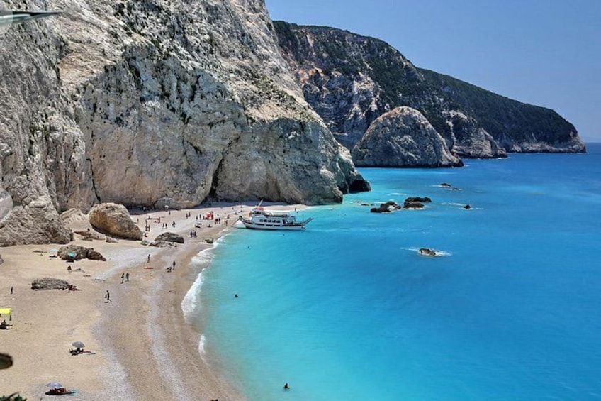 A coastal beach with clear blue waters, rocky cliffs, and a boat on the shore. 3