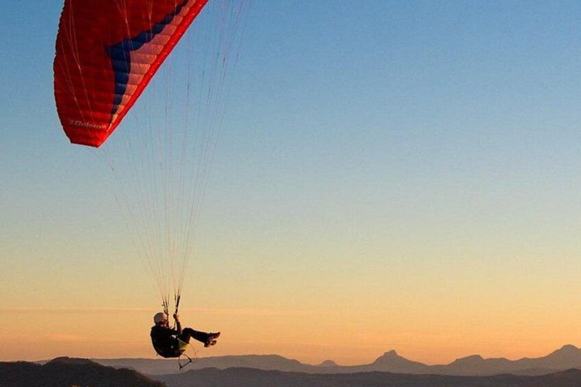A person paragliding with a red canopy, against a backdrop of a clear sky and distant mountains. 5