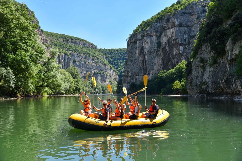 A group of people in a yellow raft on a calm river surrounded by cliffs. 2