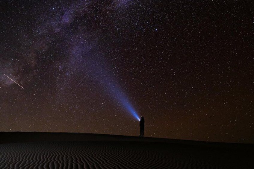 A person standing on a dune under a starry night sky with a visible Milky Way. 1