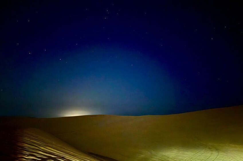 A desert landscape at night with a single light source illuminating the sand dunes. 4