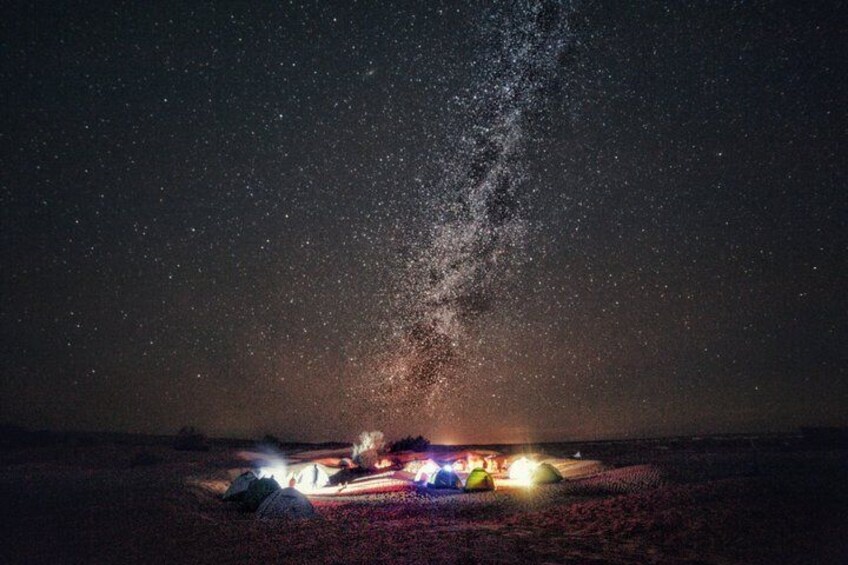 A starry night sky with a visible Milky Way and a campsite with tents and lights. 5