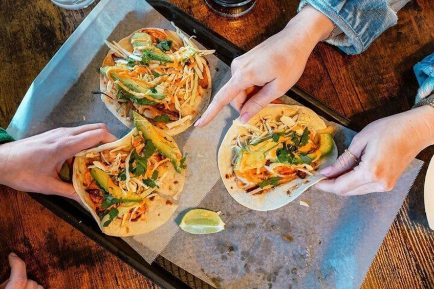 Three people preparing tacos on a wooden table. 5