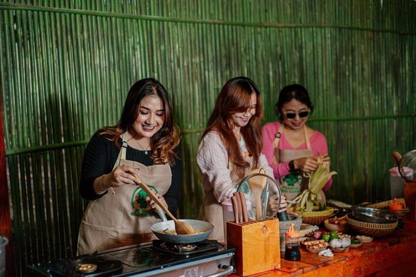 Two women cooking in a rustic kitchen with a green corrugated metal wall. 4