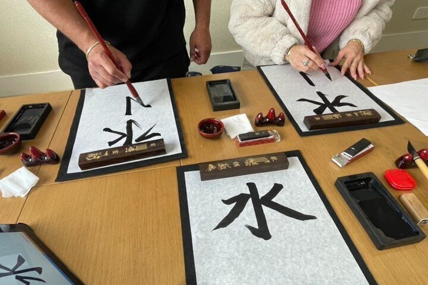 A person writing Chinese characters on a paper with a brush, surrounded by traditional calligraphy tools. 1