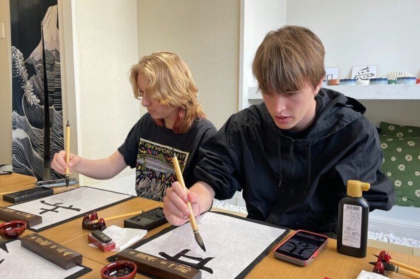 Two individuals practicing calligraphy with brushes and ink on paper, surrounded by traditional calligraphy tools. 4